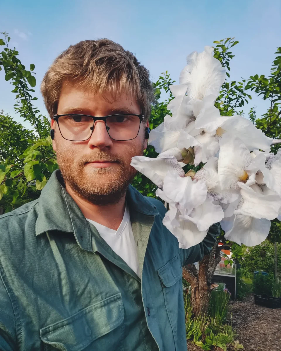 Snittblomsodlare som håller upp vita irisar bredvid huvudet.